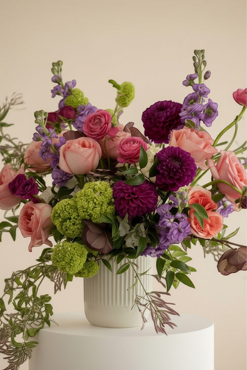 IN𝓃 Floral Studio Blush Atelier arrangement: pink roses, purple dahlias, green hydrangeas, purple stock, and ranunculus in a white ribbed vase. Size M.