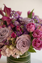 IN𝓃 Floral Studio Blush Calla arrangement with deep pink calla lilies, lavender roses, pink tulips, and hydrangeas in a glass vase.