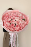 IN𝓃 Floral Studio blush pink rose bouquet wrapped in matching paper with flowing ribbons and pearl accents.