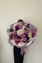 IN𝓃 Floral Studio romantic garden bouquet with lavender roses, cream hydrangeas, and deep purple dahlias in paper wrap.