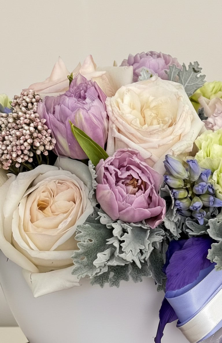 IN𝓃 Floral Studio Lavender Whisper arrangement: white roses, lavender tulips, blue hyacinths, and greenery in a white ceramic bowl with ribbon.