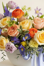 IN𝓃 Floral Studio pastel flower arrangement with roses, ranunculus, lisianthus in a white ceramic bowl with blue and white ribbons.