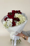 IN𝓃 Floral Studio red roses, white orchids, and hydrangeas bouquet in white paper wrap with ribbon.