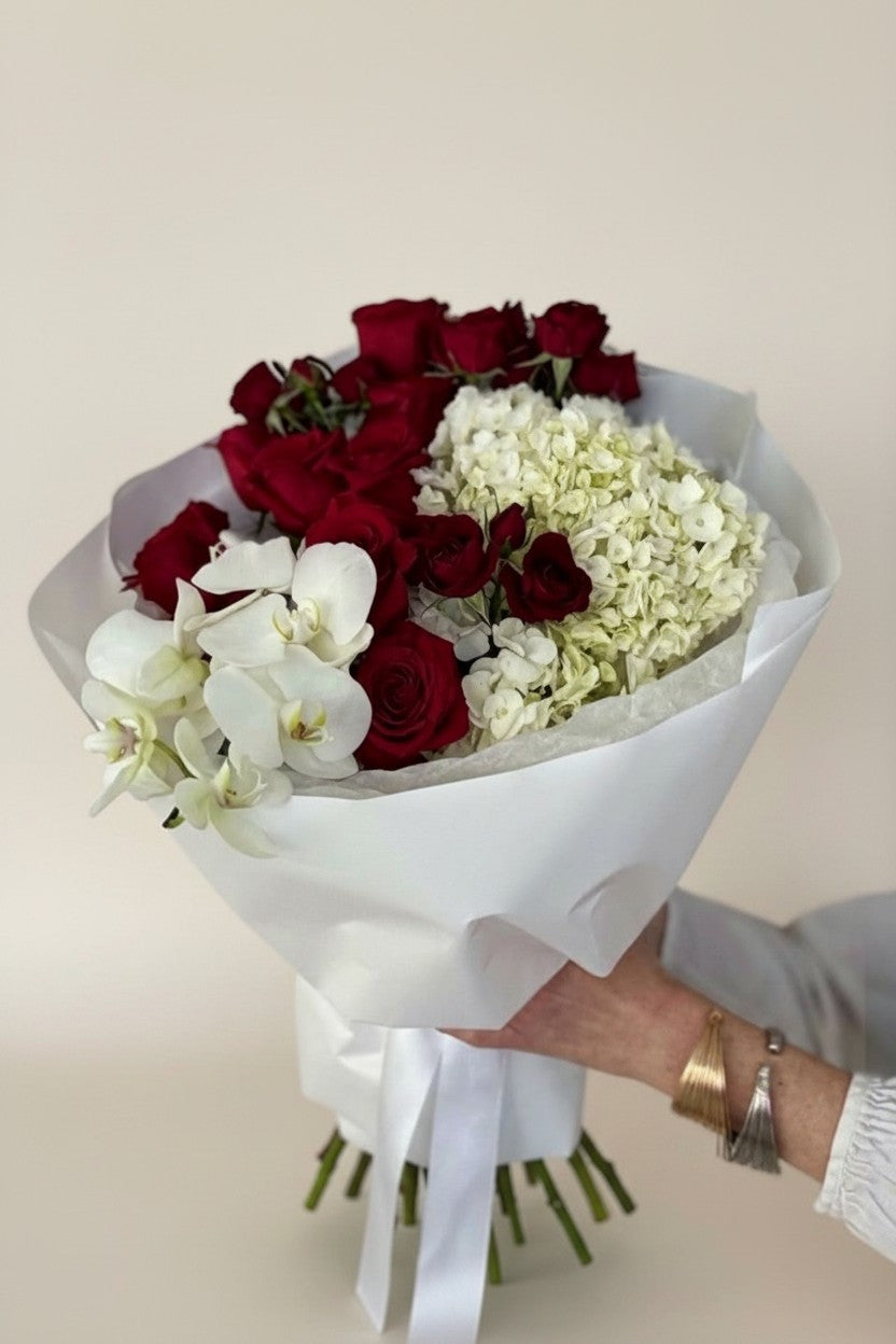 IN𝓃 Floral Studio red roses, white orchids, and hydrangeas bouquet in white paper wrap with ribbon.