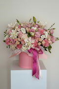 IN𝓃 Floral Studio Rosé Belle arrangement of lavender and ivory roses, white lilies, lisianthus, hydrangeas, carnations, spray roses, eucalyptus, and greens in a pink vase.