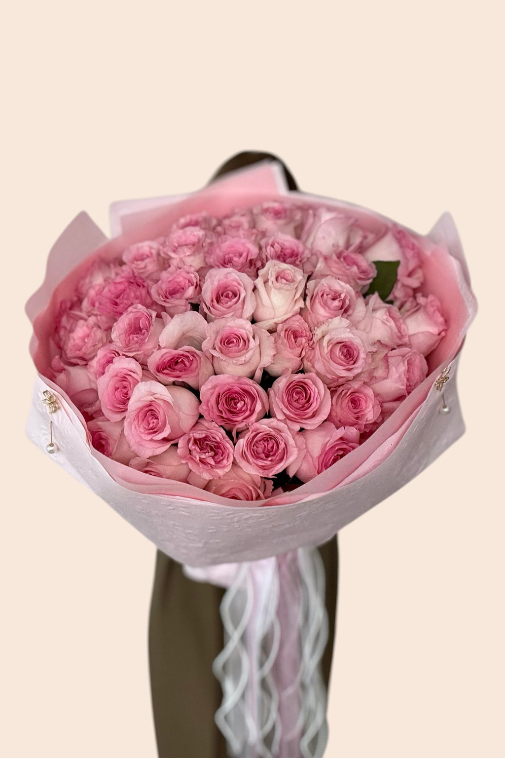 Букет ніжних рожевих троянд від IN𝓃 Floral Studio, загорнутий у рожевий папір зі стрічками та перлинами.