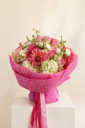 IN𝓃 Floral Studio hand-tied garden bouquet with coral dahlias, blush roses, and cream hydrangeas in pink wrap.