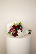 IN𝓃 Floral Studio patriotic bouquet with red roses, pink lilies, and white blooms, wrapped in white paper.