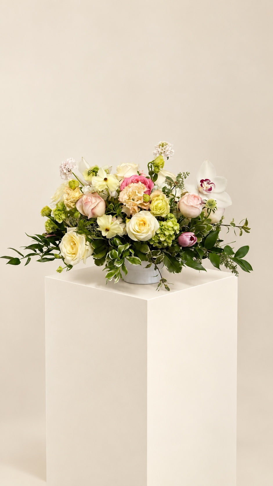Ivory roses, pink blooms and white orchids on a neutral studio pedestal