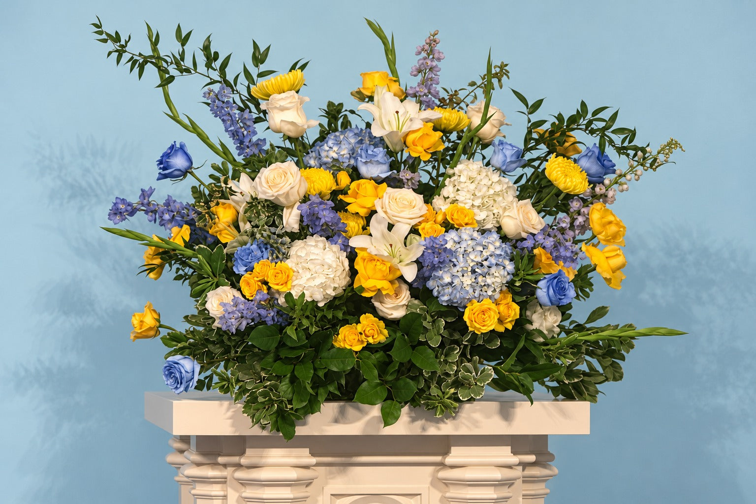Blue, white and yellow flowers on a carved cream pedestal