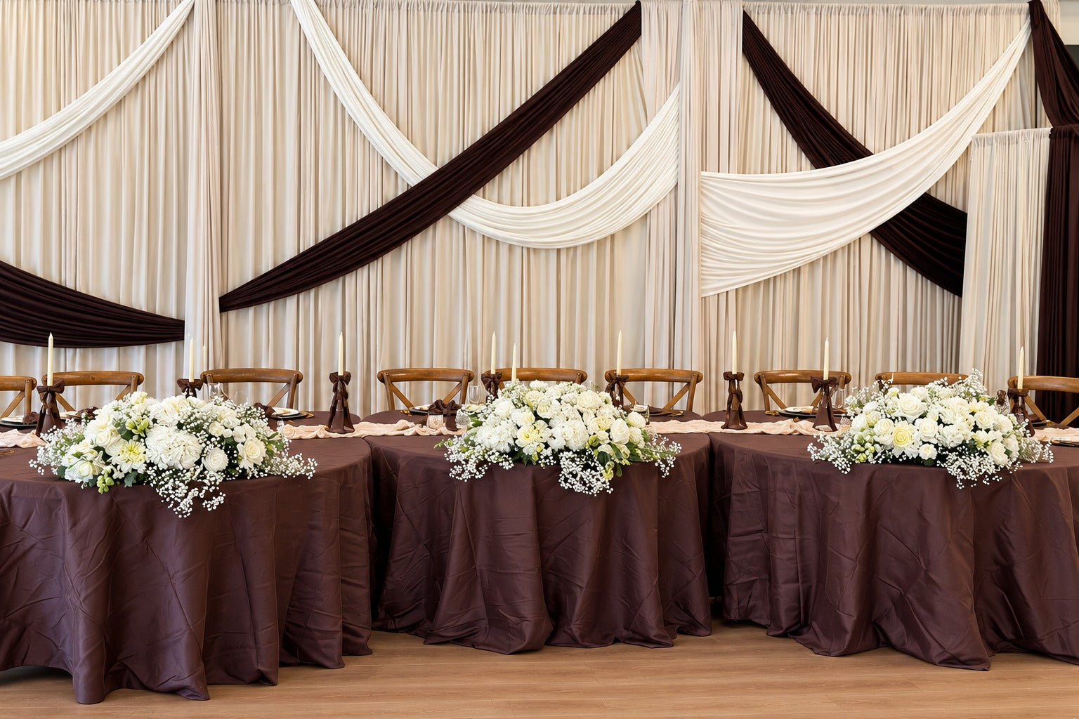 White floral arrangements across a reception table with an ivory draped backdrop