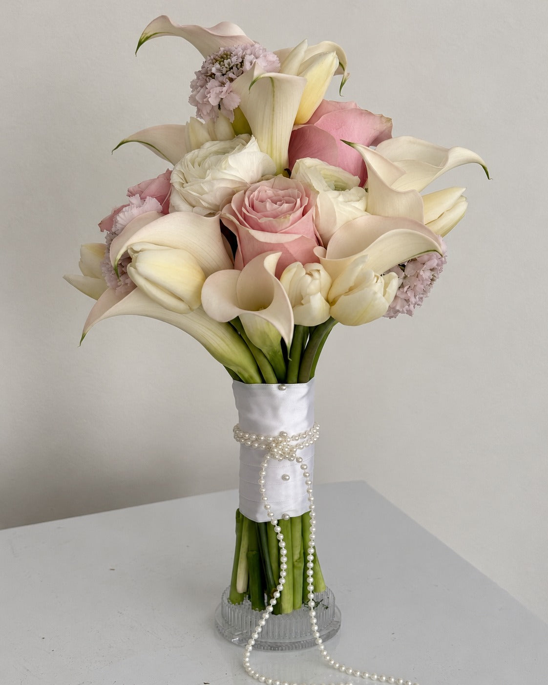 Blush roses and ivory calla lilies in a satin-wrapped bridal bouquet
